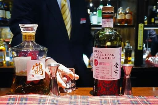 A bartender pouring a whisky for a businessman at a Japanese bar.