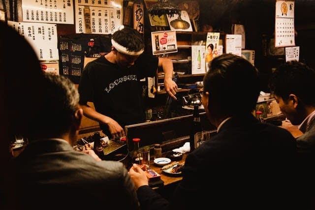 A Japanese bartender pouring drinks for colleagues at a nomikai gathering.