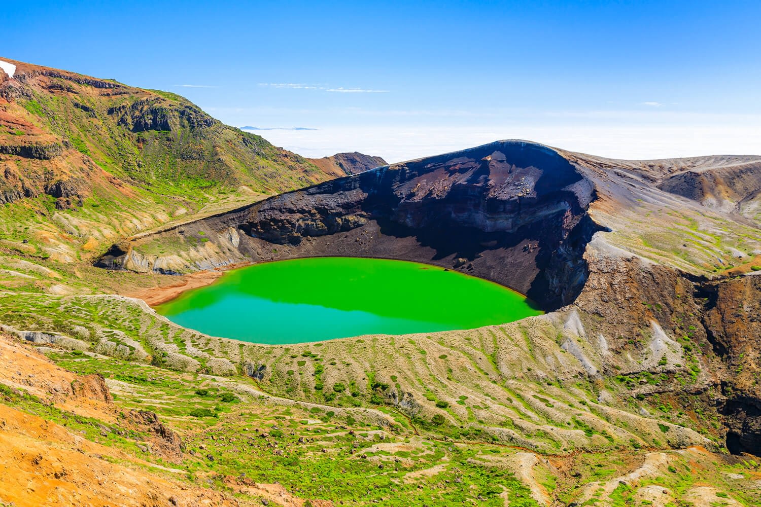 Big crater on a mountainside filled with bright green water