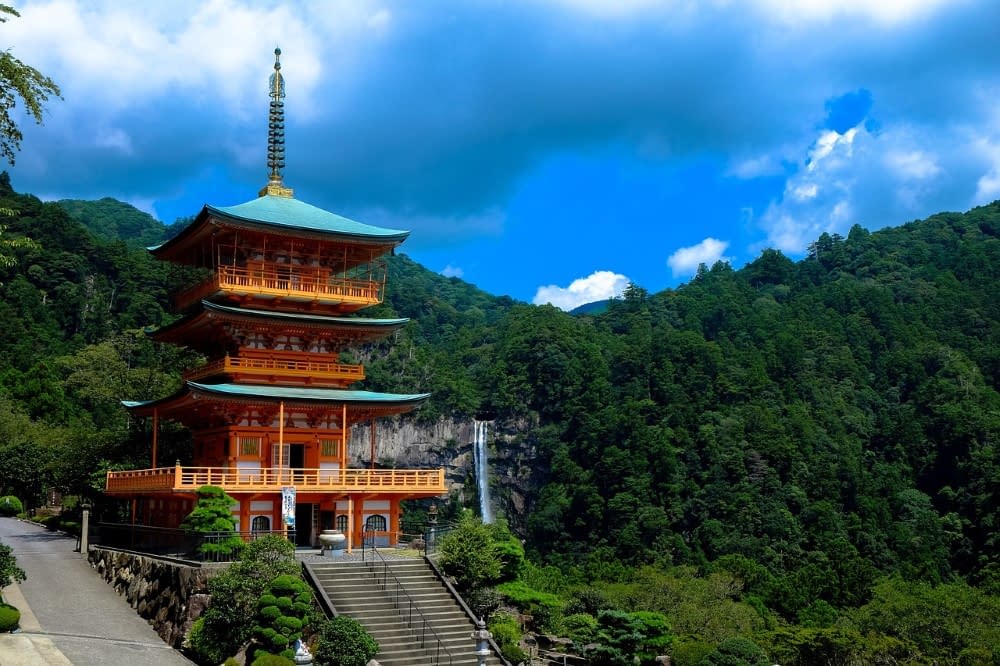A vibrant traditional Japanese building that is painted white, gold, red, and green, surrounding by hills and trees in the background