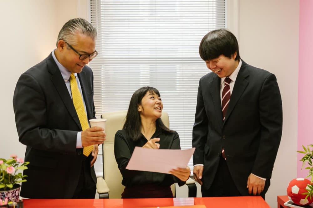 two japanese men in suits are talking to a japanese woman in a meeting room