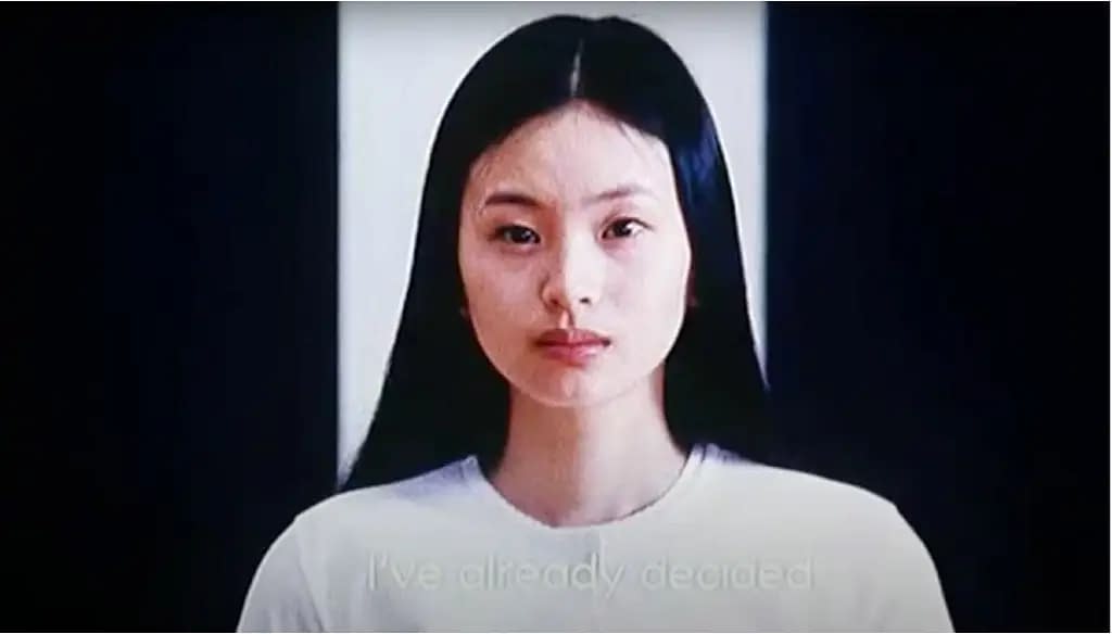 A still image from the film "Audition", which is a close-up of actress Eihi Shiina's face.