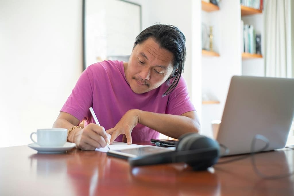 A Japanese man studying and writing at a laptop