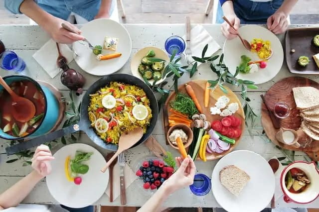 An aerial shot of a fully laden dinner table, with four people seated around a range of colourful dishes of food.