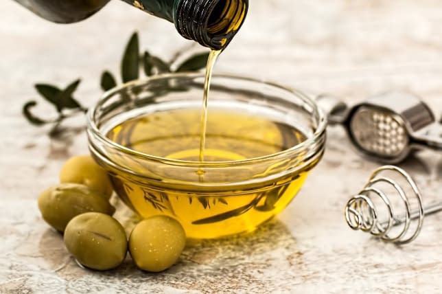 a bottle of olive oil being poured into a bowl surrounded by olives