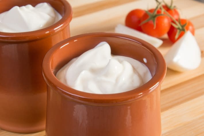 two bowls of sour cream with some tomatoes in the background