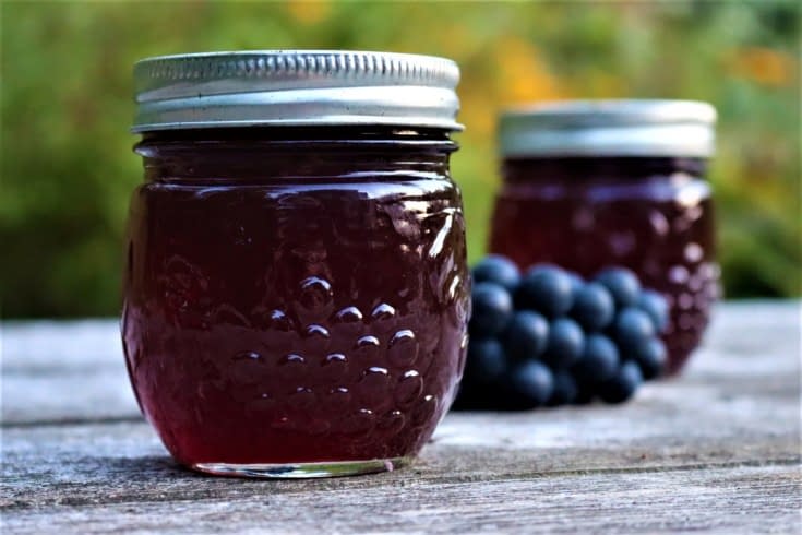 Jars of grape jelly next to a pile of grapes