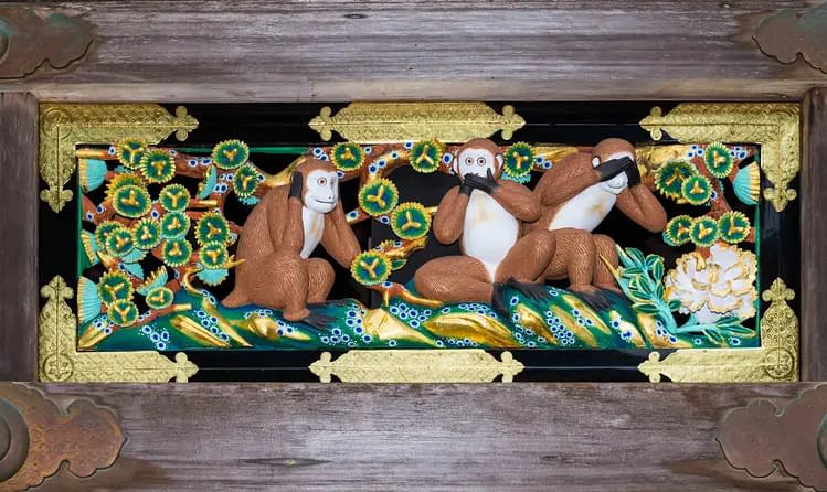 A Japanese artwork depicting the Three Wise Monkeys, carved elaborately in wood and painted in bright colours.