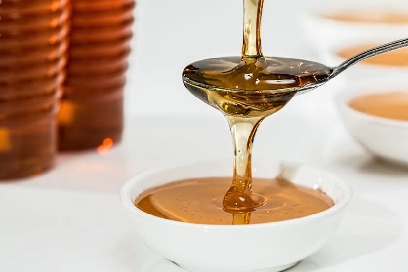 a spoon full of maple syrip dripping into a bowl with more maple syrup in