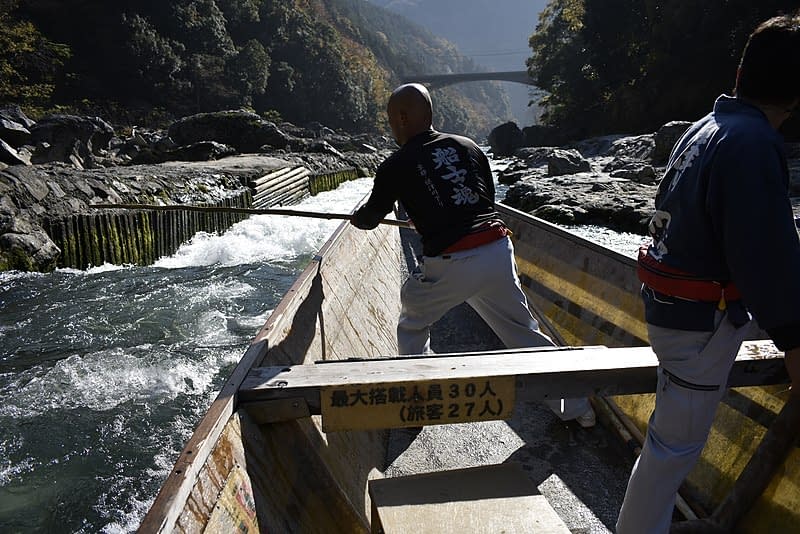 Boatmen navigating the Hozugawa river in a wooden boat.