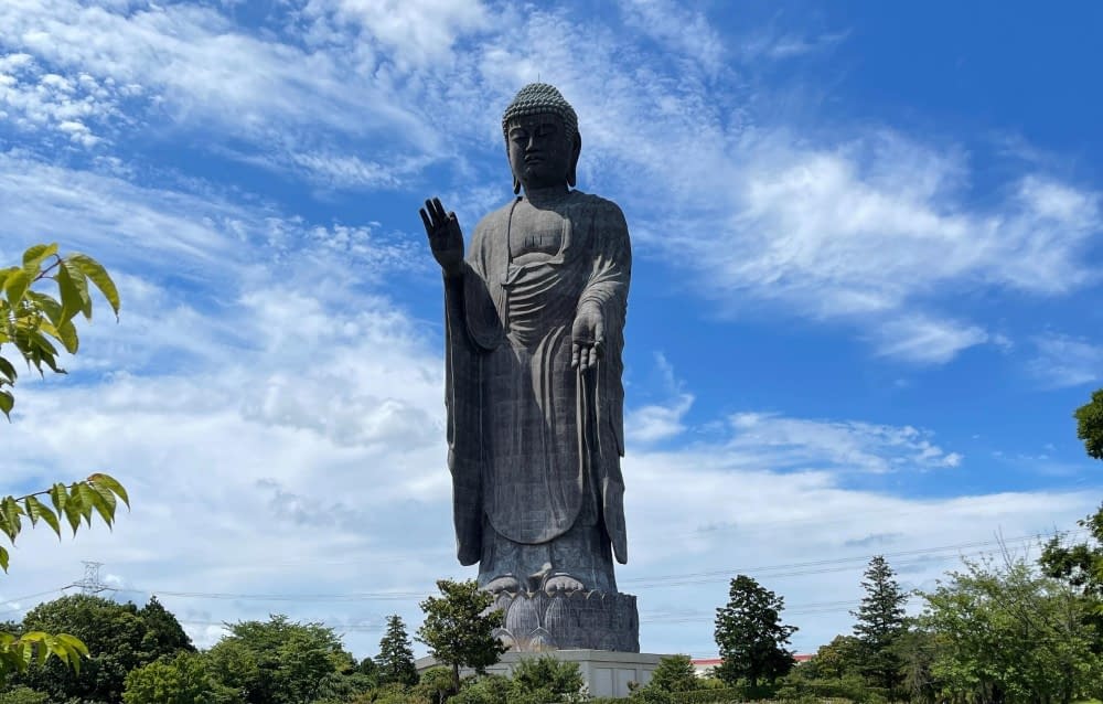 The Ushiku Daibutsu statue stood towering over the trees surrounding it with a blue cloudy sky in the background