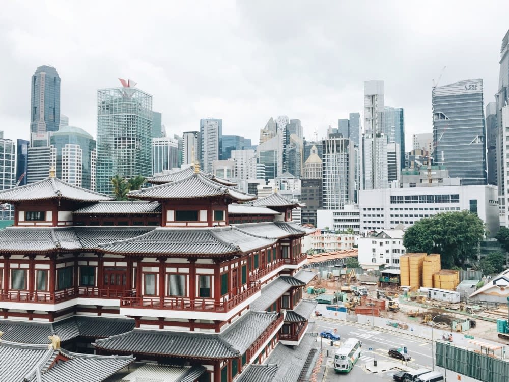 A red and white traditional Japanese building in the foreground in front of a modern city with skyscrapers in the background