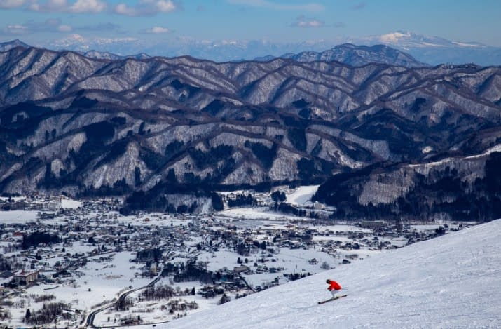 A skier in a red jacket is skiing down the hill to a ski village.