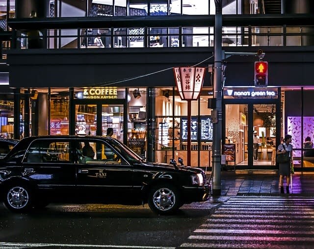 A Japanese taxi waiting at a pedestrian crossing in front of a coffee shop.