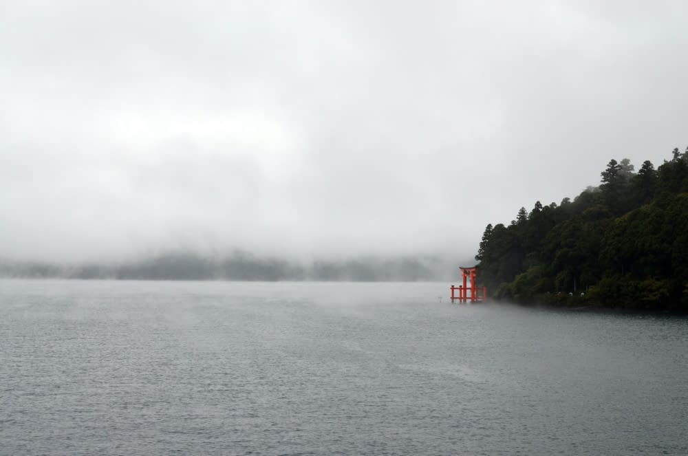 A traditional red torii gate rising from the misty waters in Hakone, Japan.