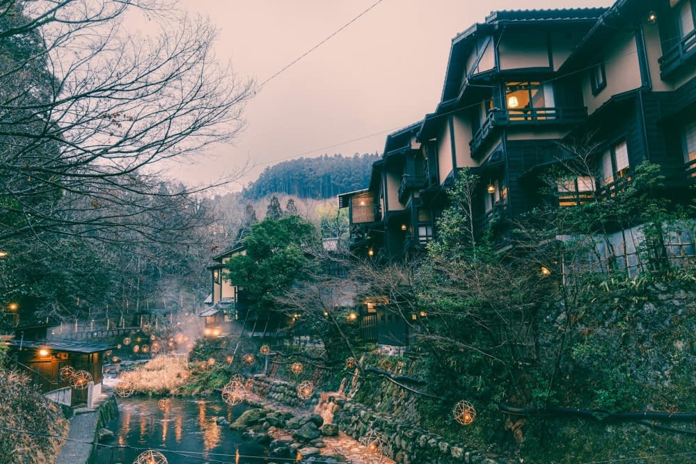 A fairy-lit river flowing through Kurokawa, Japan, surrounded by charming houses in a picturesque town setting.