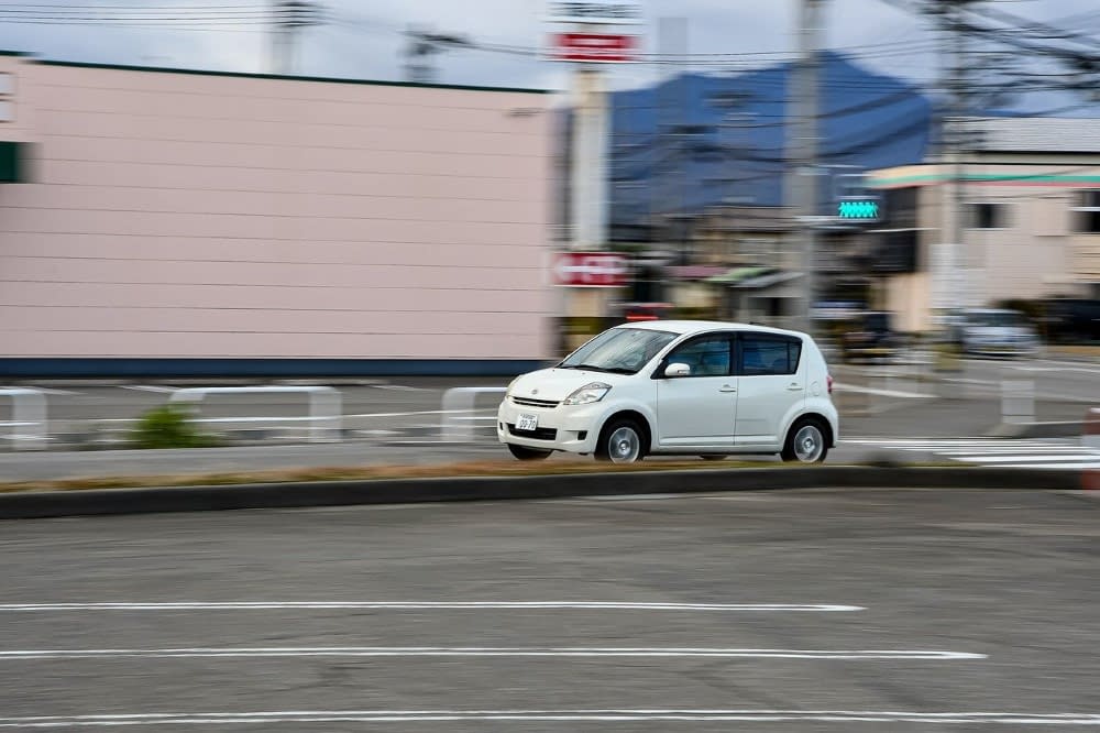 white japanese k car driving down a street