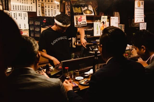 A Japanese bartender pouring drinks for colleagues at a nomikai gathering.